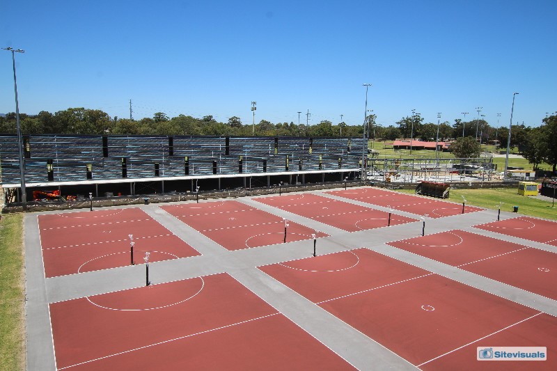 Steel frame building under construction with outdoor netball courts in foreground